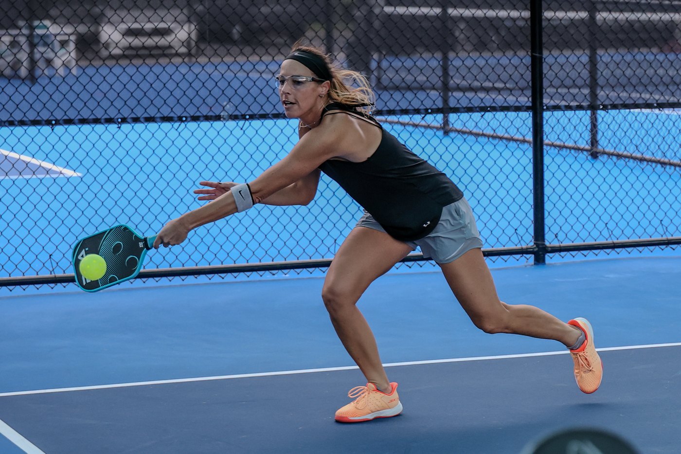 A pickleball player fully extended, reaching low for a return at the net.