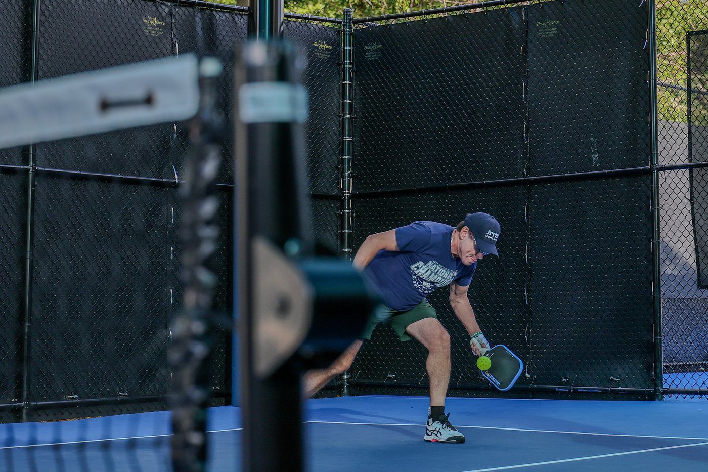 A pickleball player crouches low to return a shot near the net.