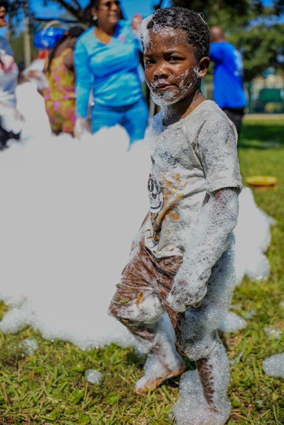 A child covered in foam glances back at the camera, families gathered behind.
